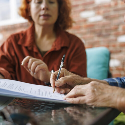 A woman watches as a man signs his will after he asked, "What Is the Best Time to Make a Will?"